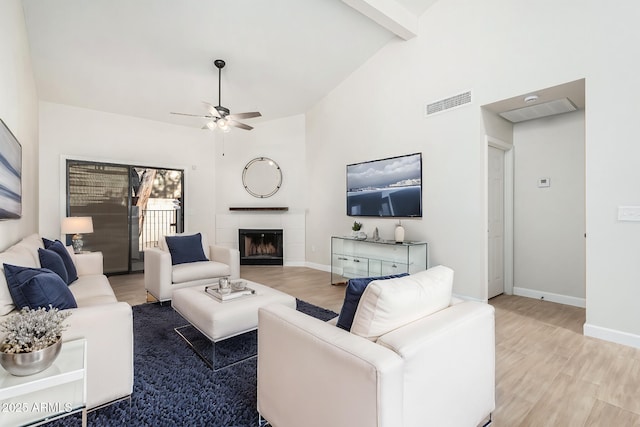 living room with hardwood / wood-style flooring, a tile fireplace, ceiling fan, beam ceiling, and high vaulted ceiling