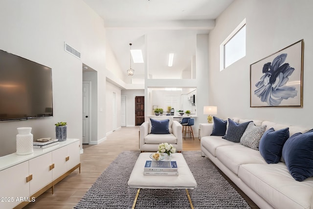 living room with a towering ceiling, a skylight, and light wood-type flooring