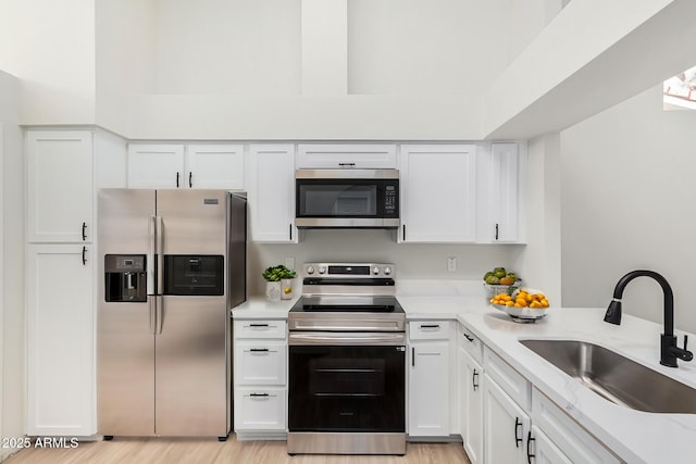 kitchen with white cabinetry, sink, light stone counters, and appliances with stainless steel finishes