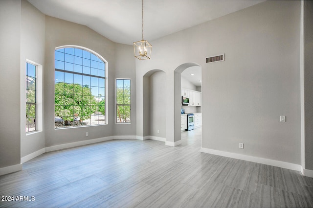 spare room with lofted ceiling, plenty of natural light, a chandelier, and light hardwood / wood-style flooring