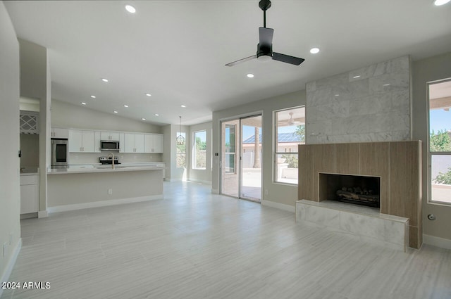 unfurnished living room with ceiling fan, lofted ceiling, plenty of natural light, and a tiled fireplace