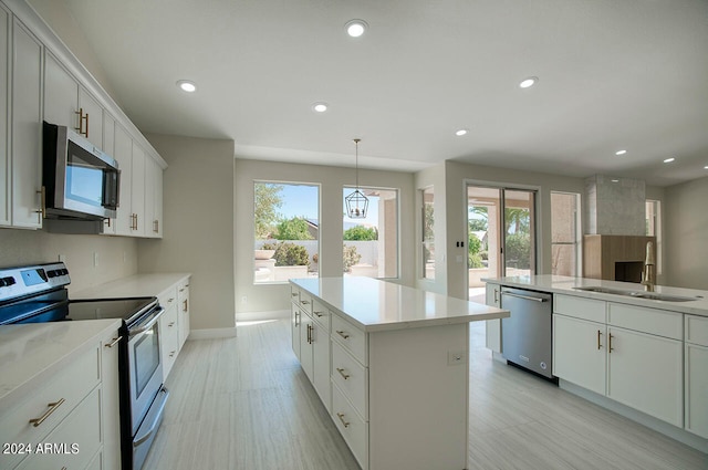 kitchen with sink, stainless steel appliances, hanging light fixtures, white cabinets, and a center island