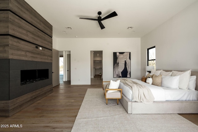 bedroom featuring wood finished floors, a fireplace, visible vents, and ceiling fan