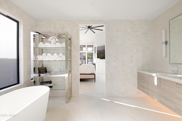 bathroom with ceiling fan, tile walls, tile patterned flooring, vanity, and a tub to relax in