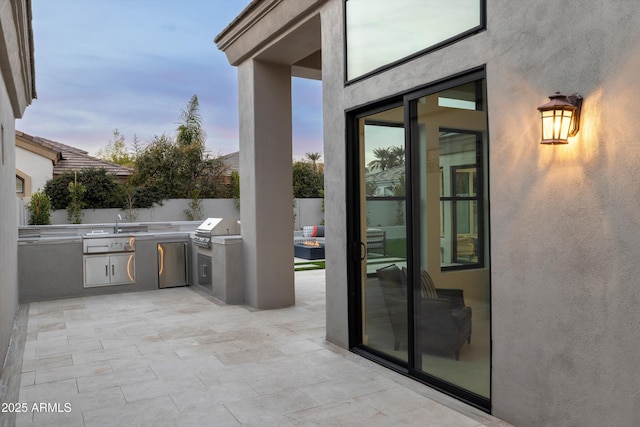 patio terrace at dusk with area for grilling and an outdoor kitchen