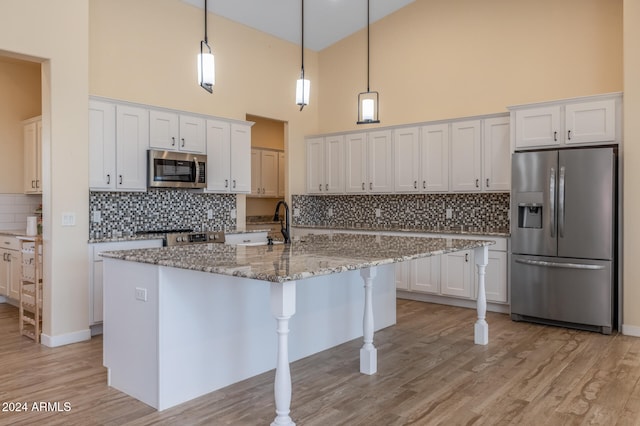 kitchen with a towering ceiling, stainless steel appliances, pendant lighting, white cabinets, and light hardwood / wood-style flooring