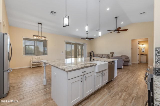 kitchen featuring appliances with stainless steel finishes, lofted ceiling, decorative light fixtures, white cabinets, and a kitchen island with sink