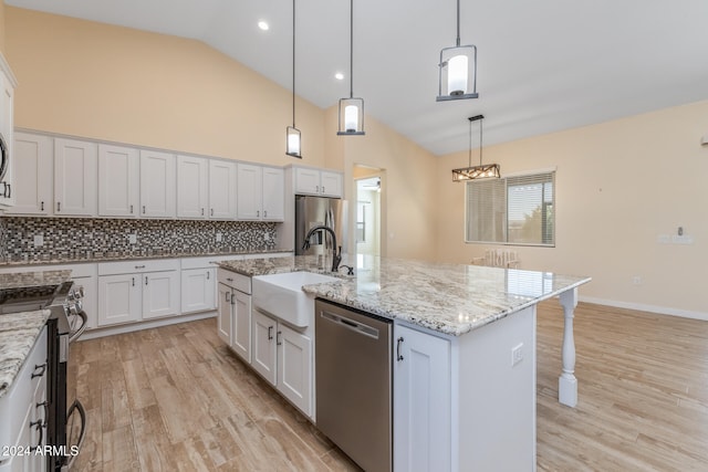 kitchen featuring light wood-type flooring, hanging light fixtures, white cabinetry, stainless steel appliances, and a kitchen island with sink