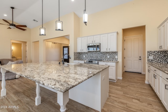 kitchen with white cabinetry, high vaulted ceiling, light hardwood / wood-style flooring, and a kitchen island with sink