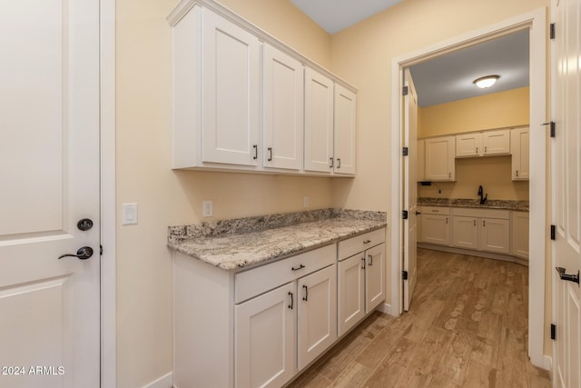 kitchen featuring white cabinetry, light stone countertops, light hardwood / wood-style flooring, and sink