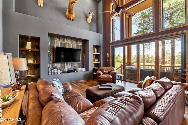 living room featuring hardwood / wood-style floors, built in features, ceiling fan, and a high ceiling