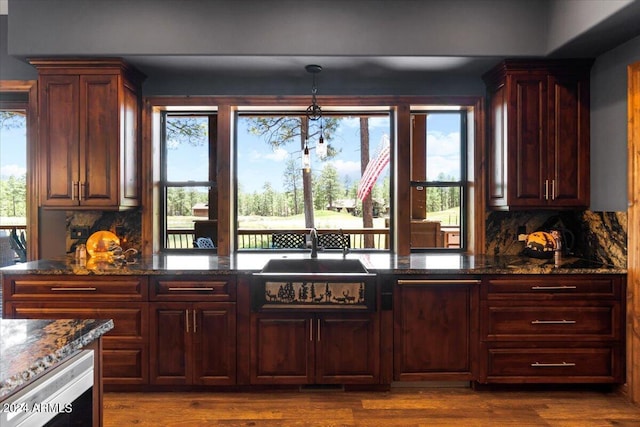 kitchen with sink, wood-type flooring, decorative backsplash, decorative light fixtures, and dark stone counters