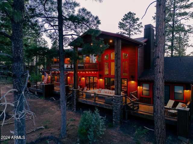 back house at dusk with an outdoor living space and a deck