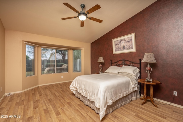 bedroom with ceiling fan, baseboards, light wood-style flooring, and vaulted ceiling