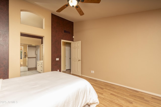 bedroom featuring visible vents, baseboards, high vaulted ceiling, light wood-style flooring, and ensuite bath