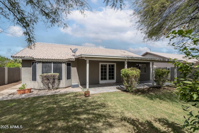 rear view of property with fence, a tiled roof, stucco siding, a lawn, and a patio