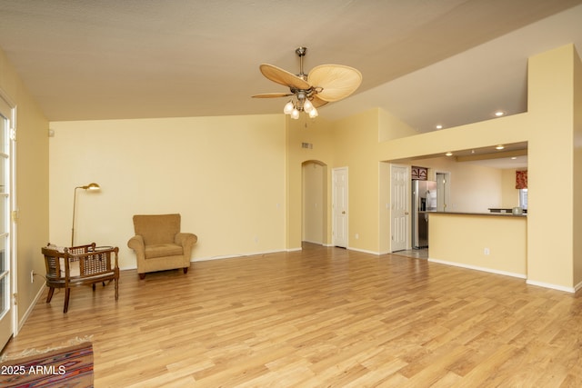 living room with arched walkways, light wood-style flooring, lofted ceiling, and ceiling fan