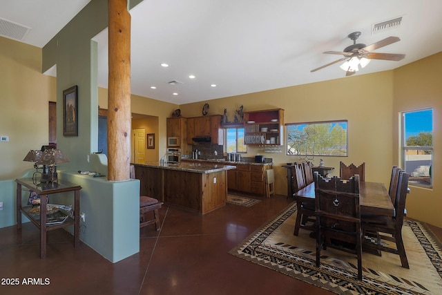 kitchen with kitchen peninsula, built in microwave, ceiling fan, and dark stone countertops