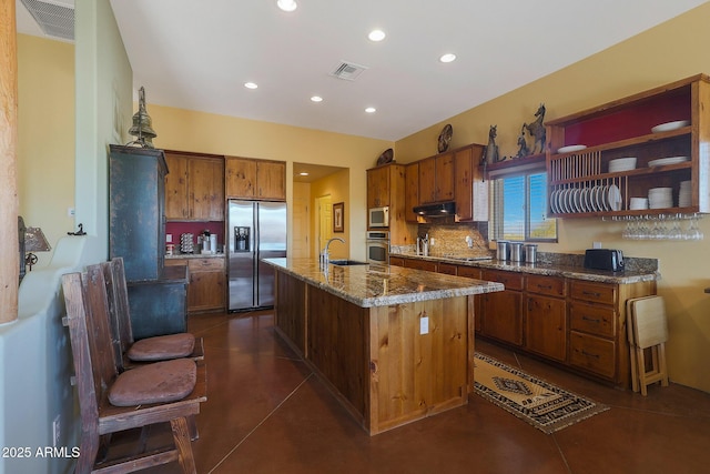 kitchen with backsplash, stone counters, sink, an island with sink, and stainless steel appliances