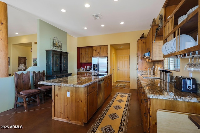 kitchen with stone counters, a center island with sink, stainless steel appliances, and sink