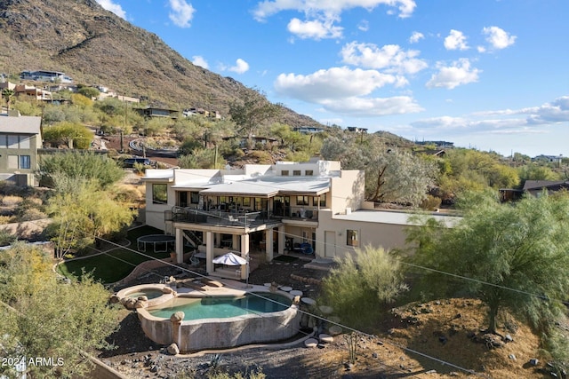 back of house with a mountain view, a swimming pool with hot tub, a balcony, and a patio area