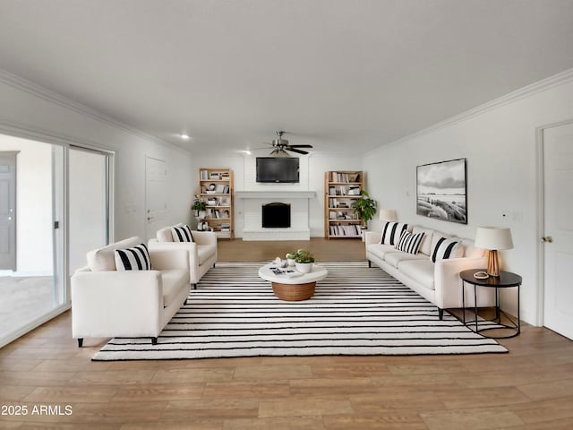 living room featuring a fireplace, ornamental molding, light wood-type flooring, and ceiling fan