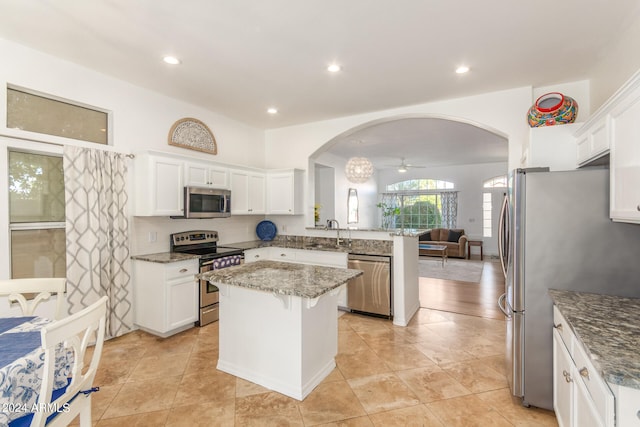 kitchen featuring light stone counters, stainless steel appliances, a kitchen island, and white cabinets