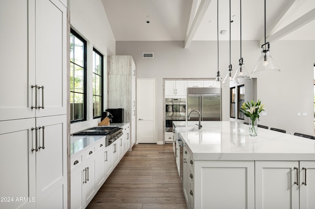 kitchen with decorative light fixtures, appliances with stainless steel finishes, an island with sink, and white cabinetry