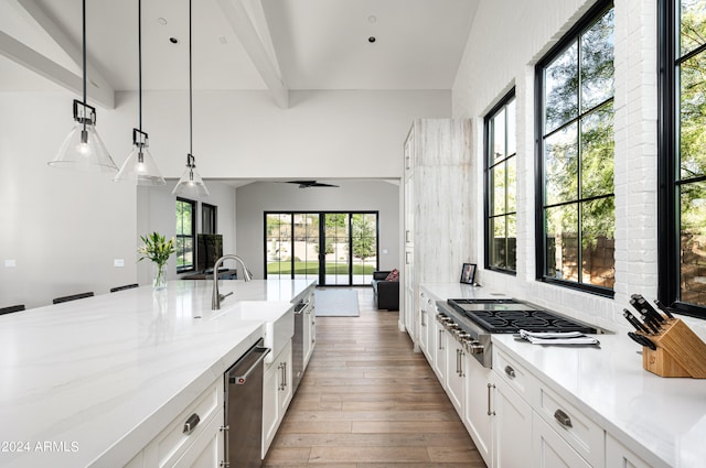 kitchen featuring decorative light fixtures, light hardwood / wood-style floors, stainless steel appliances, white cabinetry, and light stone counters