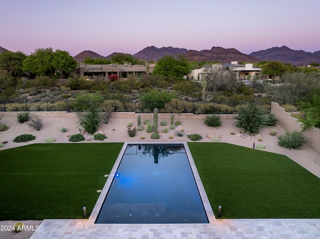 pool at dusk featuring a mountain view and a lawn