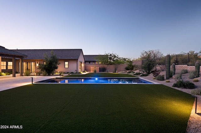 pool at dusk with a yard and a patio