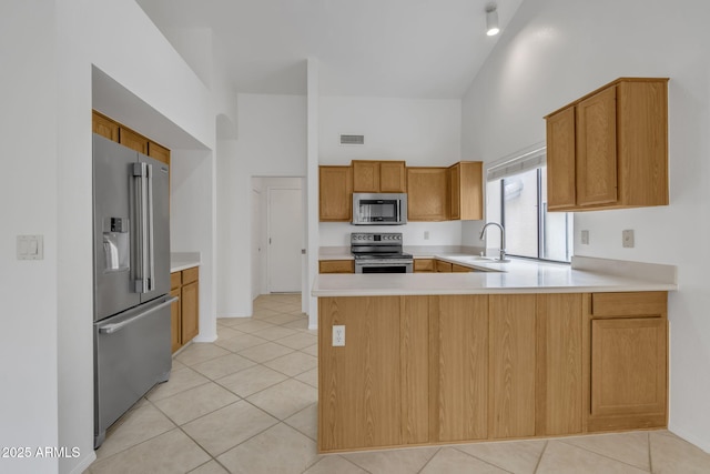 kitchen with a high ceiling, appliances with stainless steel finishes, a peninsula, and light countertops