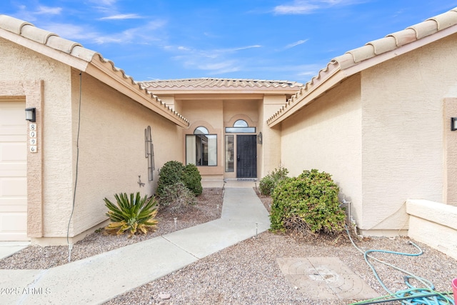 view of exterior entry featuring stucco siding, a tiled roof, and an attached garage