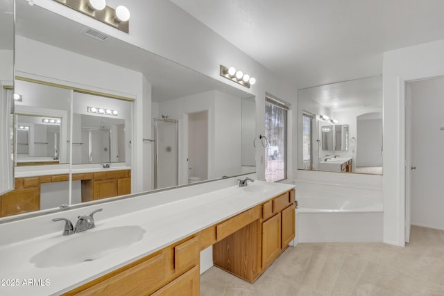 bathroom with a bath, visible vents, double vanity, and a sink