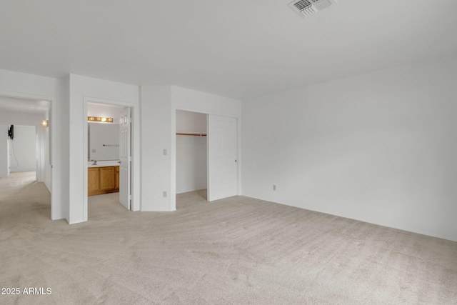 unfurnished bedroom featuring visible vents, light colored carpet, a closet, and ensuite bathroom