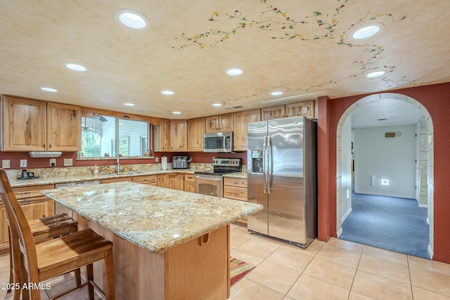 kitchen featuring a kitchen bar, light stone counters, stainless steel appliances, sink, and a kitchen island