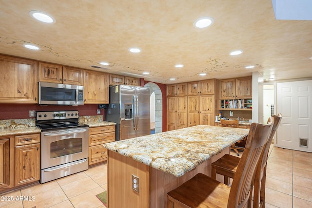 kitchen with appliances with stainless steel finishes, light stone counters, a breakfast bar, a center island, and light tile patterned flooring