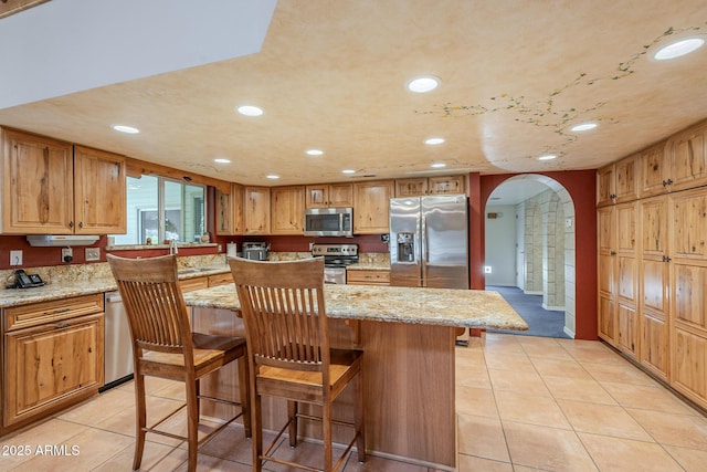 kitchen with light stone countertops, a kitchen bar, a center island, and stainless steel appliances