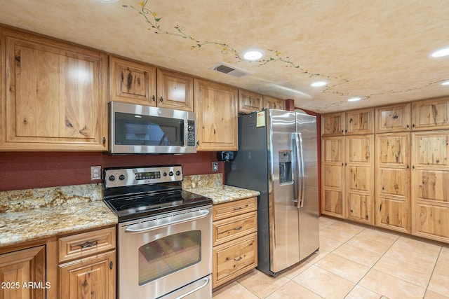 kitchen with light tile patterned flooring, light stone counters, and stainless steel appliances