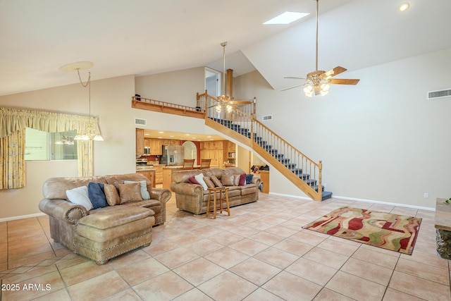 living room with a skylight, light tile patterned floors, ceiling fan with notable chandelier, and high vaulted ceiling