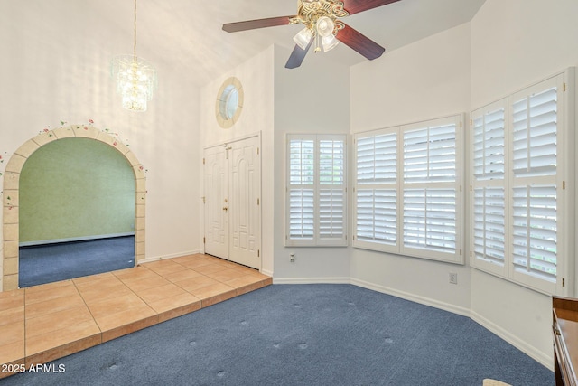 tiled foyer entrance featuring ceiling fan with notable chandelier and high vaulted ceiling