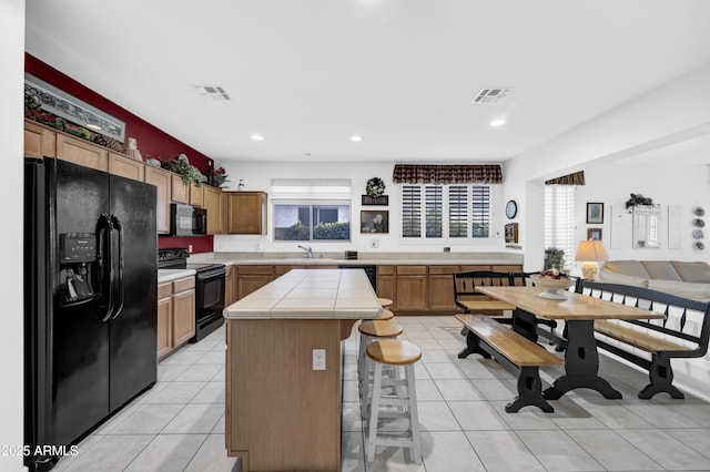 kitchen featuring sink, light tile patterned floors, a breakfast bar, black appliances, and a kitchen island