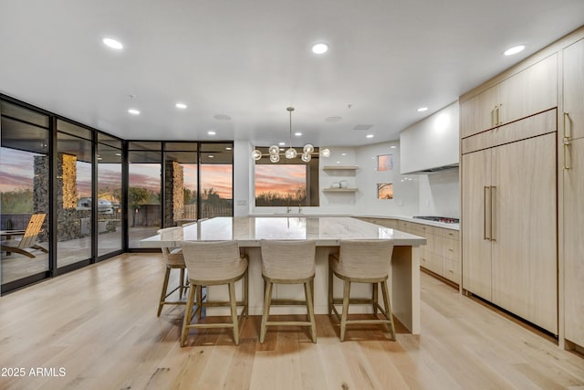 kitchen featuring gas cooktop, hanging light fixtures, light stone countertops, a kitchen island, and light wood-type flooring