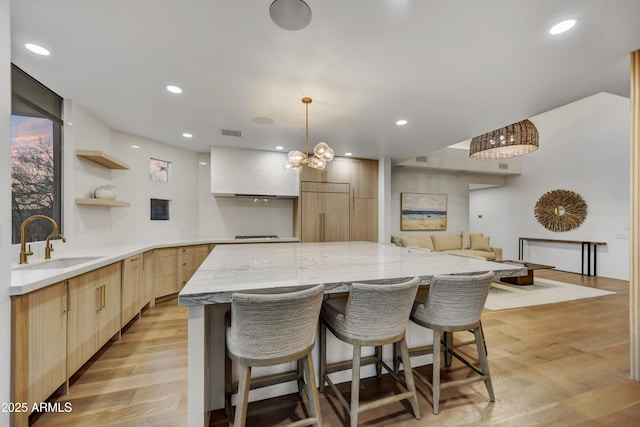 kitchen with sink, white cabinets, a center island, paneled built in fridge, and light wood-type flooring