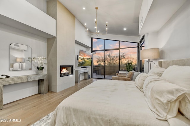 bedroom featuring an inviting chandelier, a towering ceiling, a fireplace, and light hardwood / wood-style floors