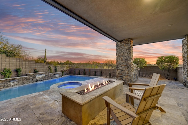 pool at dusk featuring pool water feature, an outdoor fire pit, an in ground hot tub, and a patio area