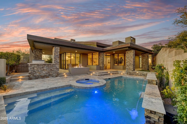 pool at dusk featuring a patio, exterior kitchen, pool water feature, and an in ground hot tub