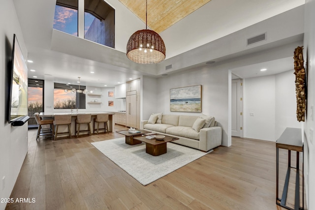 living room featuring light hardwood / wood-style floors, a chandelier, and a high ceiling