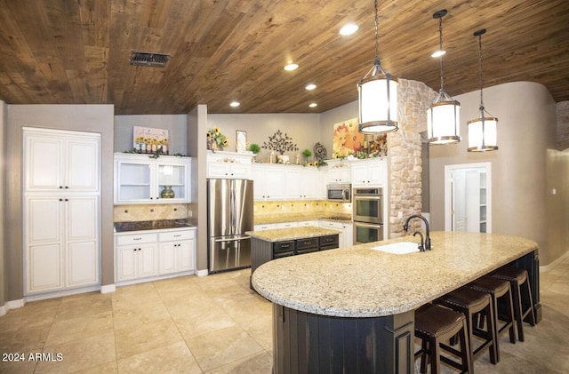 kitchen featuring lofted ceiling, white cabinets, hanging light fixtures, appliances with stainless steel finishes, and a kitchen island with sink