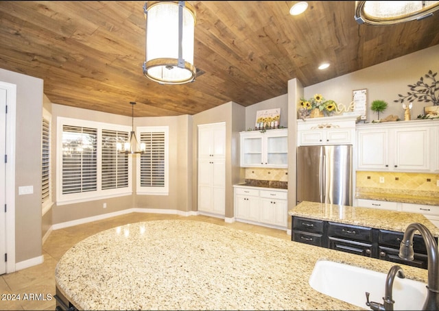 kitchen featuring white cabinets, stainless steel refrigerator, vaulted ceiling, sink, and decorative light fixtures